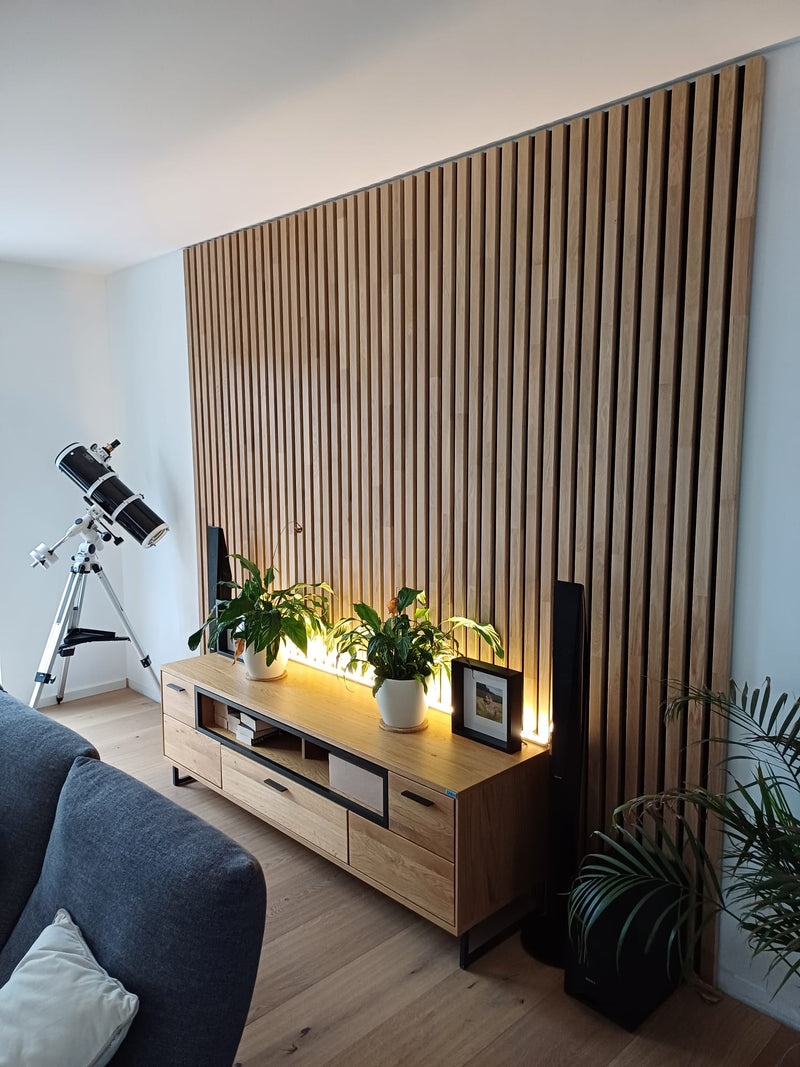 Wohnwand mit Akustikpaneelen aus Eiche Natur geölt, davor ein Sideboard mit Fernseher, Pflanzen und warmem Licht